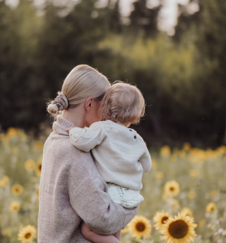 A child in a woman's arms in a sunflower field.