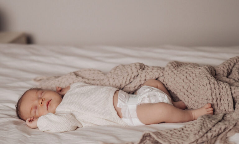 A baby sleeping on their back on the bed.
